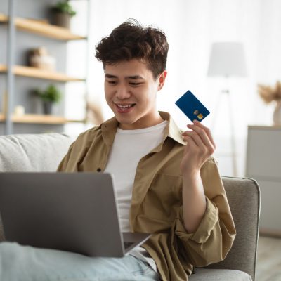 Smiling asian guy showing credit card at home